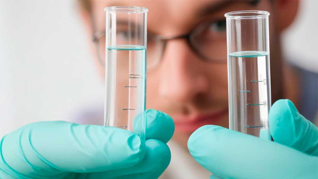 Dos pipetas con un líquido transparente que parece agua en primer plano y la cara de un chico de gafas difuminada al fondo