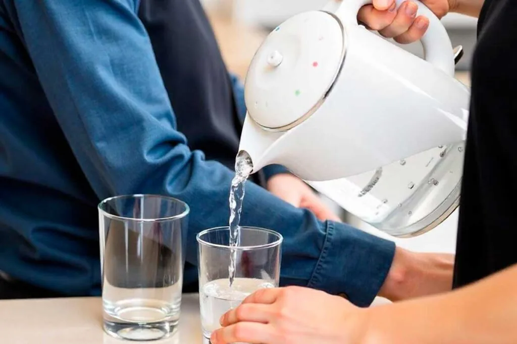 Persona echando agua en un vaso desde una jarra de agua con filtro